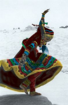 a woman is dancing in the snow with her colorful dress and headdress on