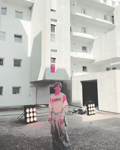 a woman with pink paint on her face standing in front of a white apartment building