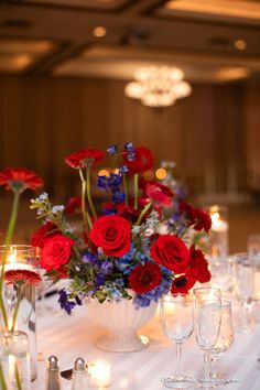 a vase filled with red and blue flowers sitting on top of a table next to wine glasses