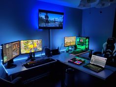 three computer monitors sitting on top of a desk in front of a flat screen tv