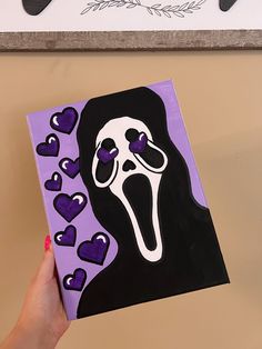 a person holding up a purple and black paper with a ghost on it's face