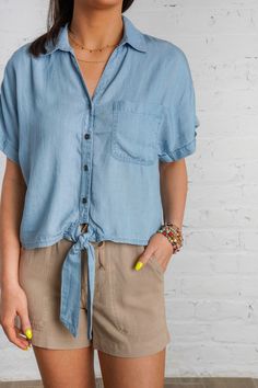 Ride the waves of style with our Drifting Tides Top. This blue chambray top features a button down front, a tie detail, and a front pocket, perfect for a casual yet chic look. The short cuffed drop sleeves and collared neckline add a touch of charm, while the soft chambray material provides ultimate comfort. Pair with our Sand Dune Shorts and Sunbeam Raffia Mules to complete the look! This top is lightweight, non-sheer, and has a loose boxy fit. 100% Tencel Brand- Be Cool Model is 5'5" and is we Beach Denim Short Sleeve Top, Denim Beach Top With Short Sleeves, Spring Button-up Top With Tie Sleeves, Spring Tie Sleeve Button-up Top, Collared Denim Top For Summer, Casual Short Sleeve Blouse With Tie Sleeves, Casual Tops With Tie Sleeves For Day Out, Casual Blouse With Tie Sleeves, Summer Chambray Collared Denim Top