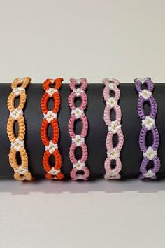 five bracelets are lined up on a black piece of paper, each with different colors and designs