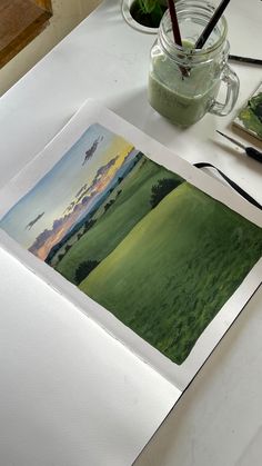 an open book sitting on top of a white table next to a jar filled with paint