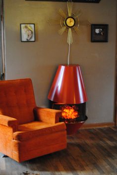 an orange chair sitting in front of a fire place next to a clock on the wall