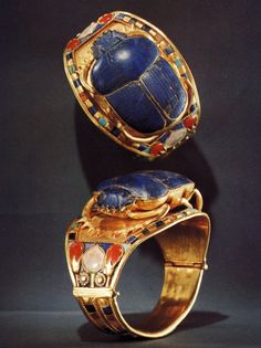 two gold rings with blue and red stones on them, one in the shape of an egg