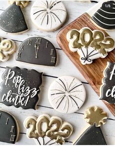 cookies decorated with gold and black icing are arranged on a white wooden surface next to a cutting board