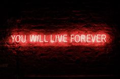 a neon sign that says you will live forever on a brick wall in the dark