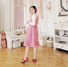 a woman in a red and white checkered dress is standing in a room with wood floors