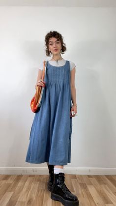 a woman standing in front of a white wall wearing a blue dress and black boots