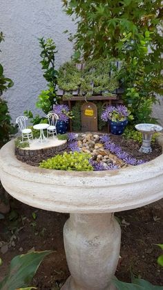 there is a small garden in the middle of a stone birdbath with trees and flowers around it