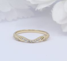 a gold wedding band with white diamonds on it and a flower in the foreground