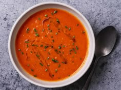 a white bowl filled with red sauce and garnished with chopped green herbs next to a spoon