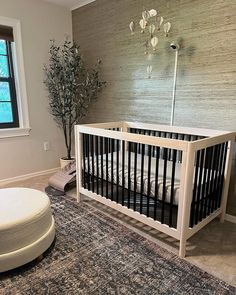 a baby crib in the corner of a room next to a round ottoman and potted plant