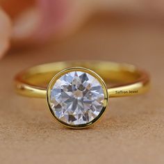 a close up view of a diamond in a yellow gold ring on a brown surface