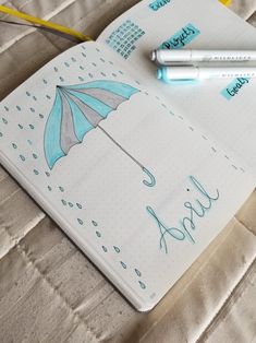 a notebook with an umbrella drawn on it and two pens laying next to the book