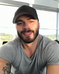 a man with a beard wearing a gray shirt and a black hat smiles at the camera