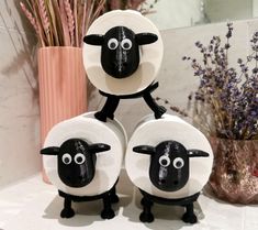 three black and white sheep standing next to each other in front of a vase with purple flowers