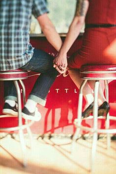 two people sitting on stools in front of a red wall with the words love written on it