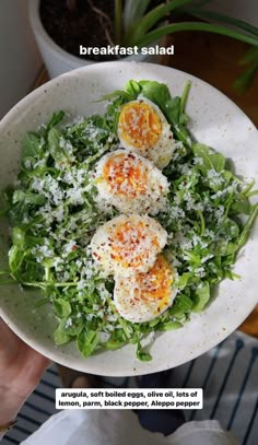 a person holding a white bowl filled with salad and hard boiled eggs on top of lettuce