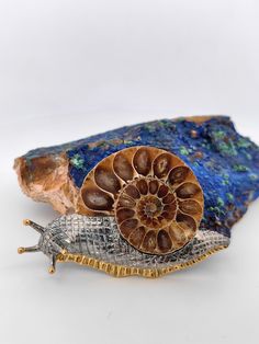 a snail sitting on top of a rock next to a piece of blue and gold