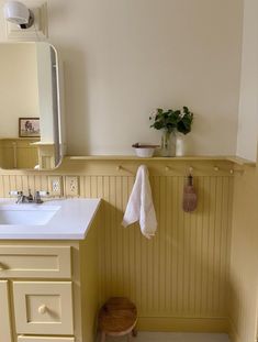 a white sink sitting under a bathroom mirror next to a wooden stool with a plant on it