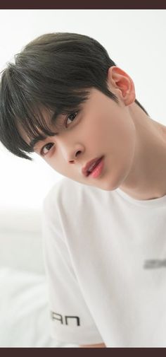 a young man with black hair wearing a white t - shirt and looking at the camera