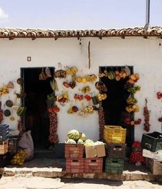 fruit and vegetables are displayed in front of a white building with black shutters on the doors