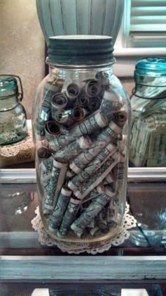 a glass jar filled with lots of money sitting on top of a table next to other jars