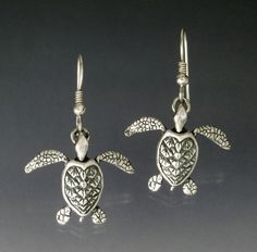 a pair of silver sea turtle earrings with hearts and leaves on the ear ends, set against a gray background