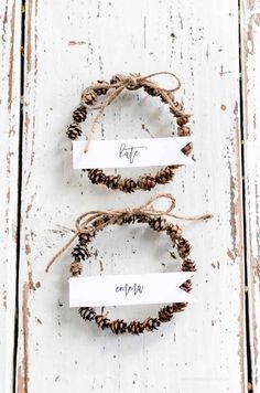 three pine cones tied to each other with name tags on them, sitting on a white wooden surface