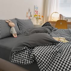 an unmade bed with black and white checkered sheets, pillows and a stuffed animal