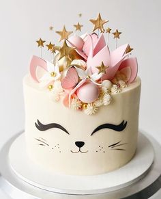 a white cake with pink and gold decorations on it's face is sitting on a plate