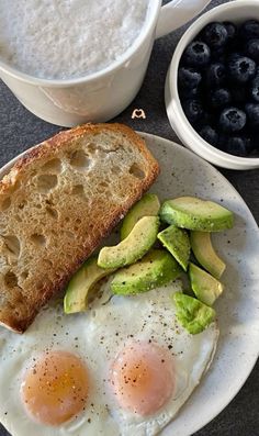 two eggs and toast on a plate with blueberries next to it, along with a bowl of yogurt