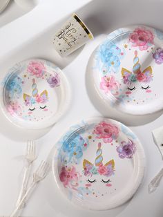 three paper plates with unicorn faces and flowers painted on them next to a bottle of wine