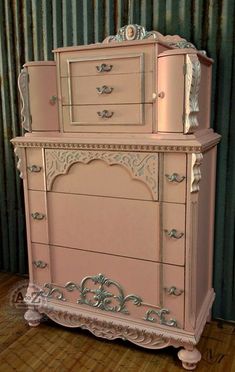 an antique pink dresser with ornate carvings on the top and bottom drawers, in front of a corrugated wall