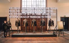 two men standing in front of a display with suits on mannequins and words written across them