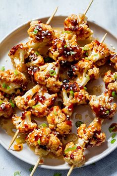 chicken skewers with sauce and green onions on a white plate, ready to be eaten