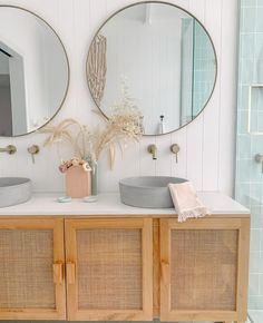 two round mirrors on the wall in a bathroom with wood cabinets and wicker drawers