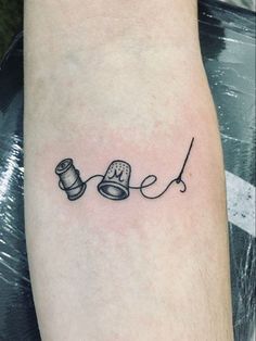 a tattoo on the arm of a person with a sewing needle and spool