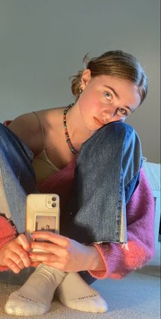 a woman sitting on the floor with her legs crossed and holding a cell phone in front of her face