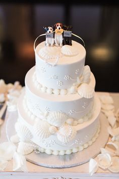 a three tiered wedding cake decorated with sea shells and small figurines on top