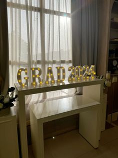 the word graduation is lit up in front of a window with sheer curtains and flowers