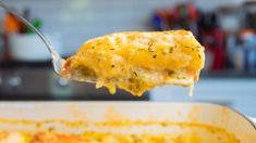 a spoon full of cheesy potatoes being lifted from a casserole dish