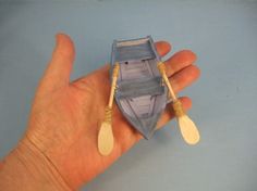 a hand holding a small toy boat with two paddles on it's side