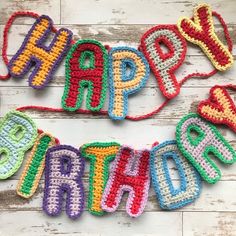 crocheted happy birthday letters are laid out on a white wooden surface with string