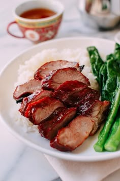 a white plate topped with meat and veggies next to a cup of tea