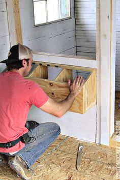 a man in red shirt and jeans kneeling on floor next to wooden box with drawers