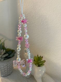 a pink and white beaded necklace hanging from a hook on a shelf next to a potted plant