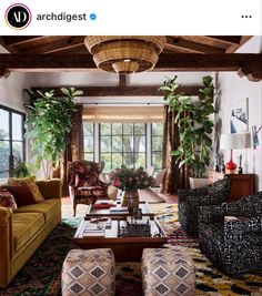 a living room filled with lots of furniture and plants on top of the tables in front of large windows